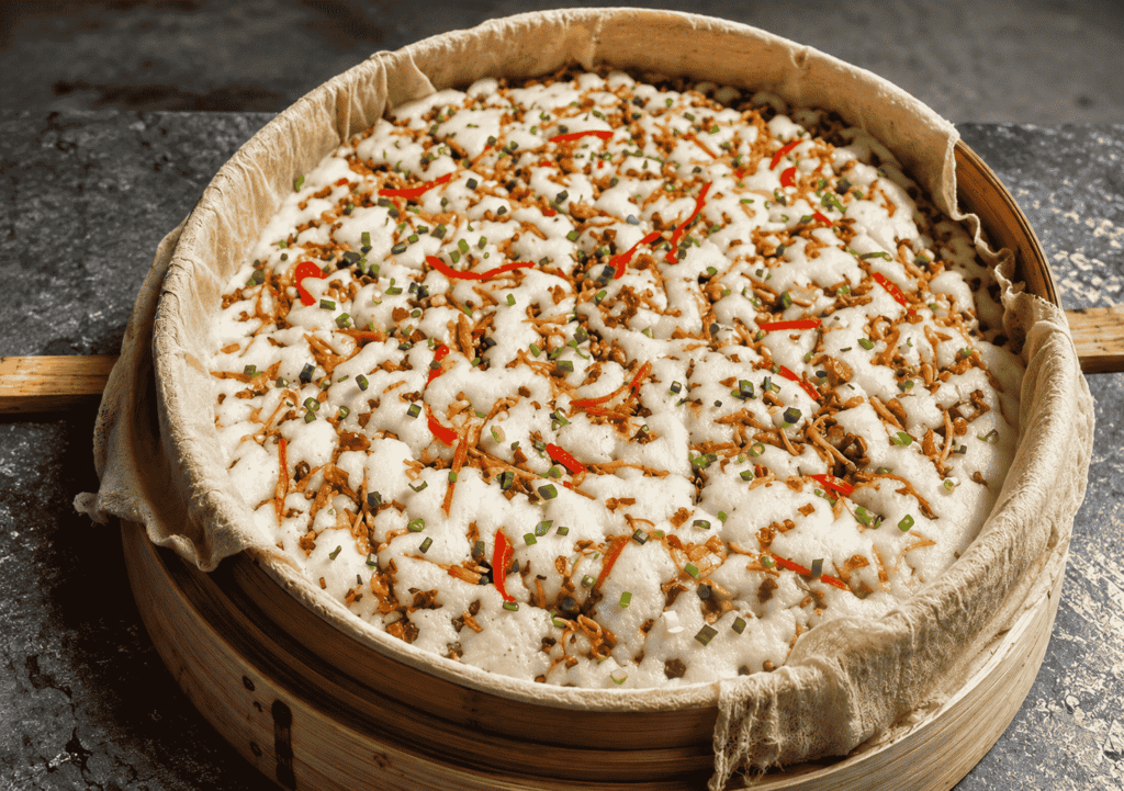 Changshan Pei Gao served in a bamboo steamer with savory toppings, red pepper strips, and chopped scallions.