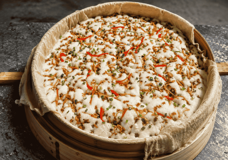 Changshan Pei Gao served in a bamboo steamer with savory toppings, red pepper strips, and chopped scallions.